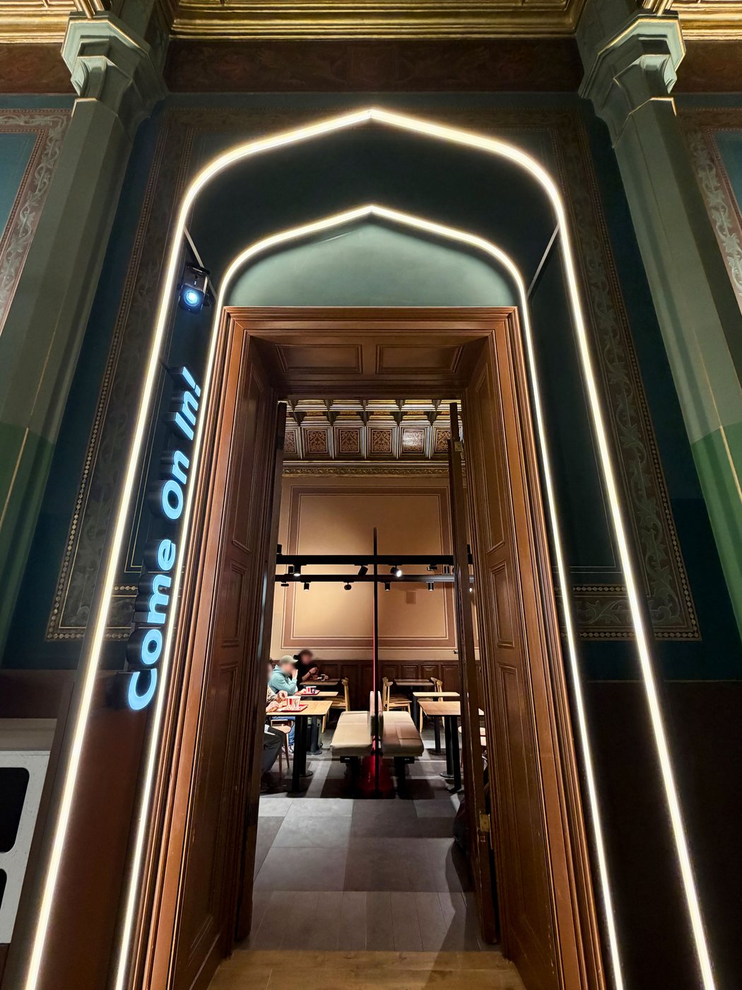 KFC Wrocław Główny — illuminated ogee arch entry portal set against the station's historic painted walls