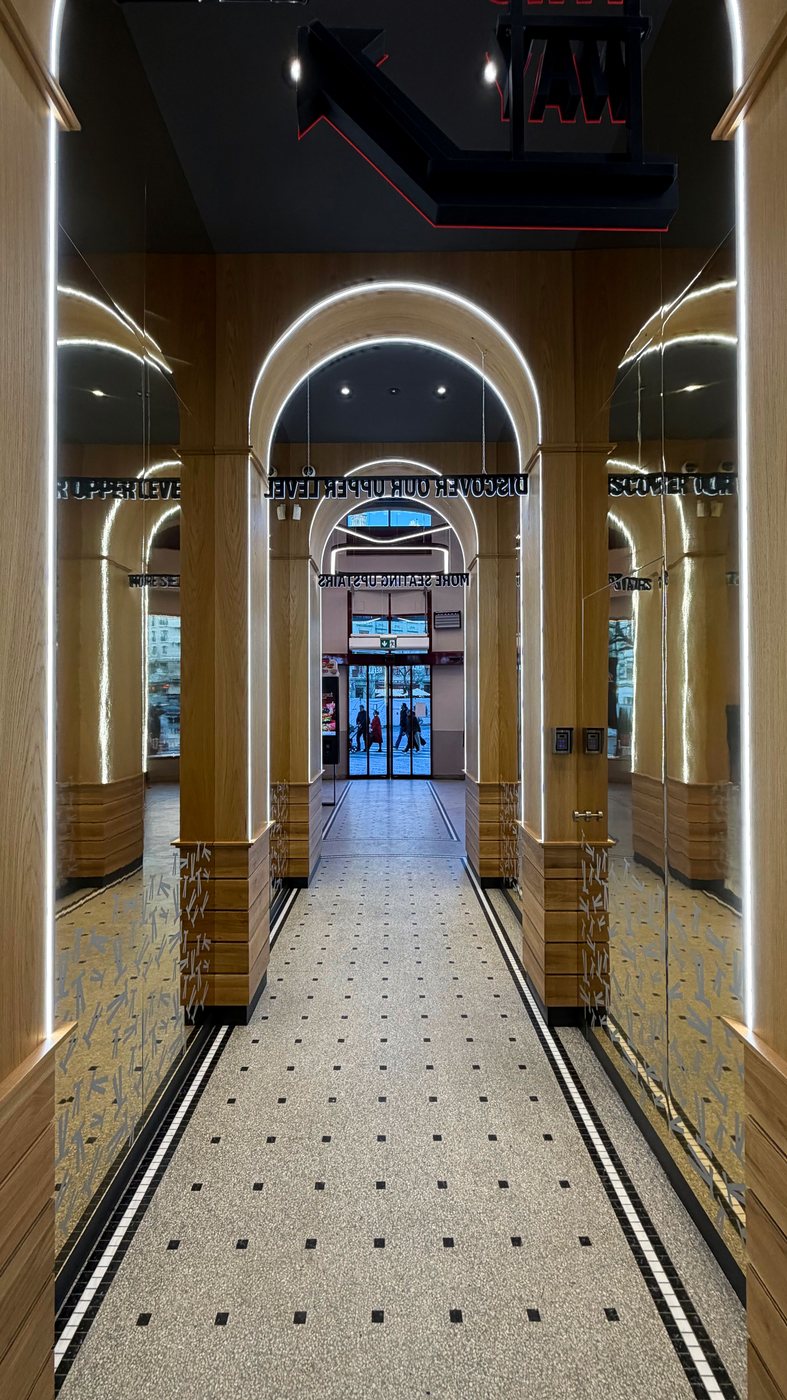 KFC VN40 — mirrored oak arcade with illuminated arches and mosaic floor leading to the entrance